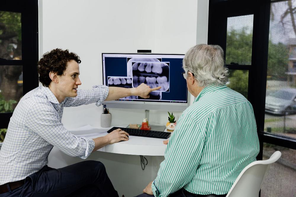 A man at a desk, focused on a computer screen, discussing dental crowns and bridges in Clayfield