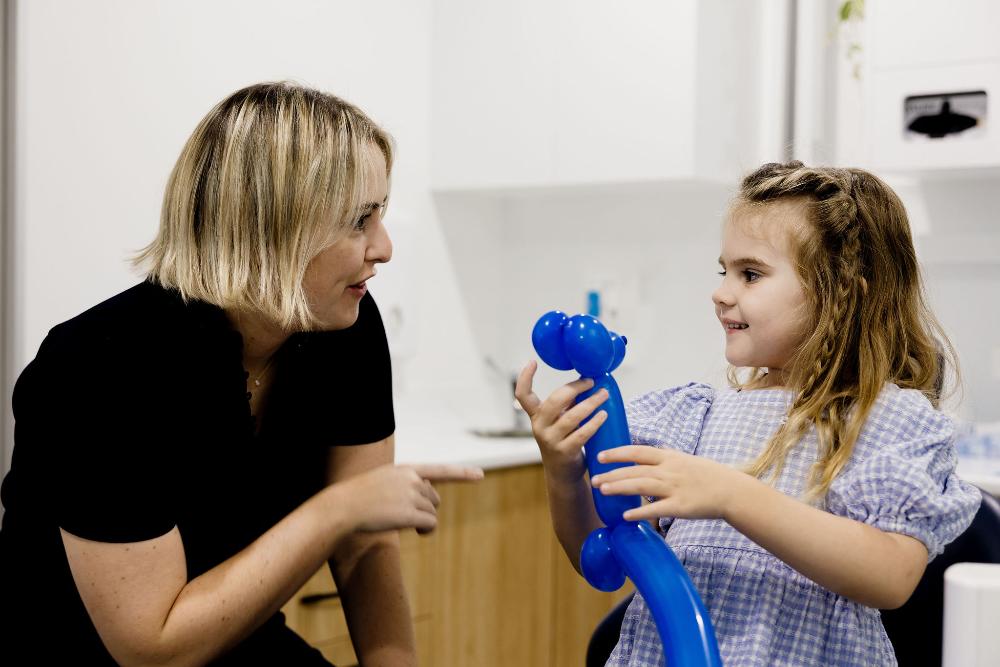A woman and a little girl joyfully playing with a blue toy at Children's Dentistry in Clayfield.