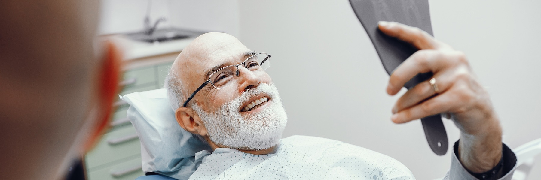 Smiling older man in dental chair reviewing treatment information on a clipboard with dentist